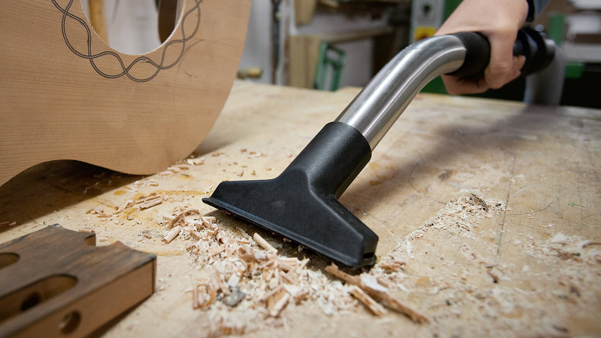 Una persona aspira restos de madera del banco de trabajo con el aspirador seco y húmedo STIHL SE 122 E y la boquilla aspiradora universal