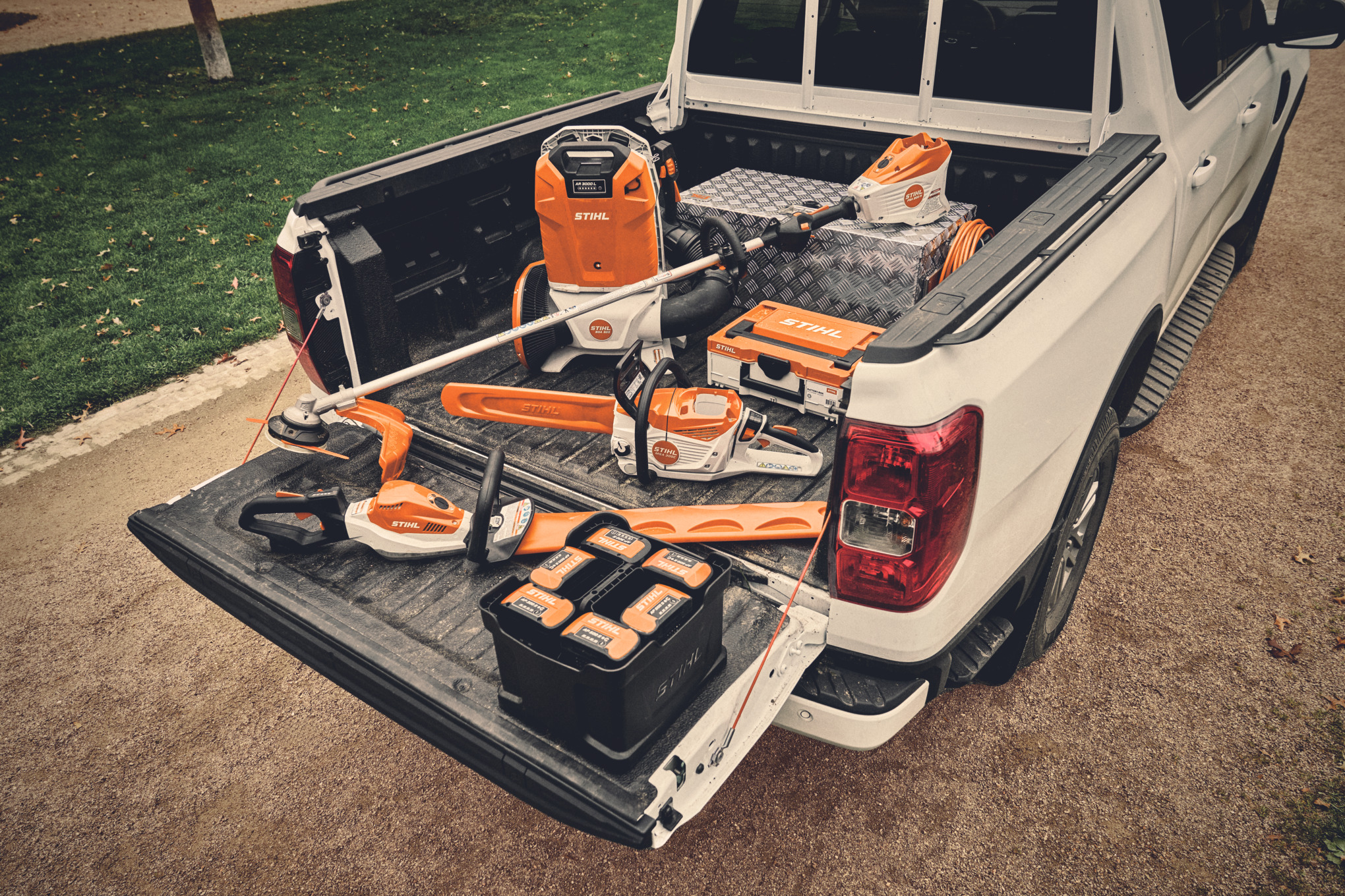 Varias herramientas eléctricas a batería y baterías compatibles del sistema STIHL AP en la plataforma de carga de un vehículo.  