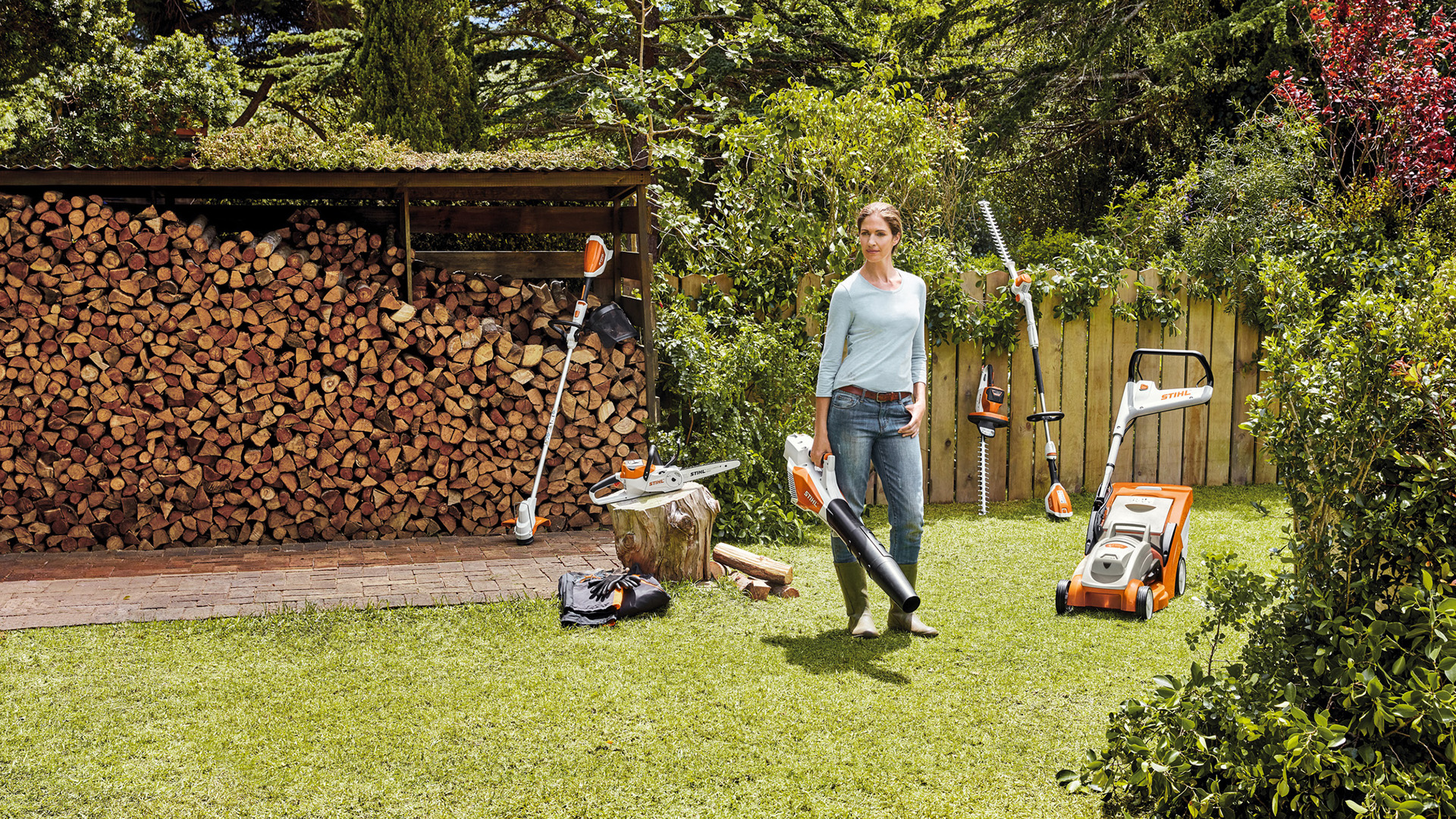 Una mujer de pie en un jardín con una selección de máquinas de batería del sistema STIHL AK