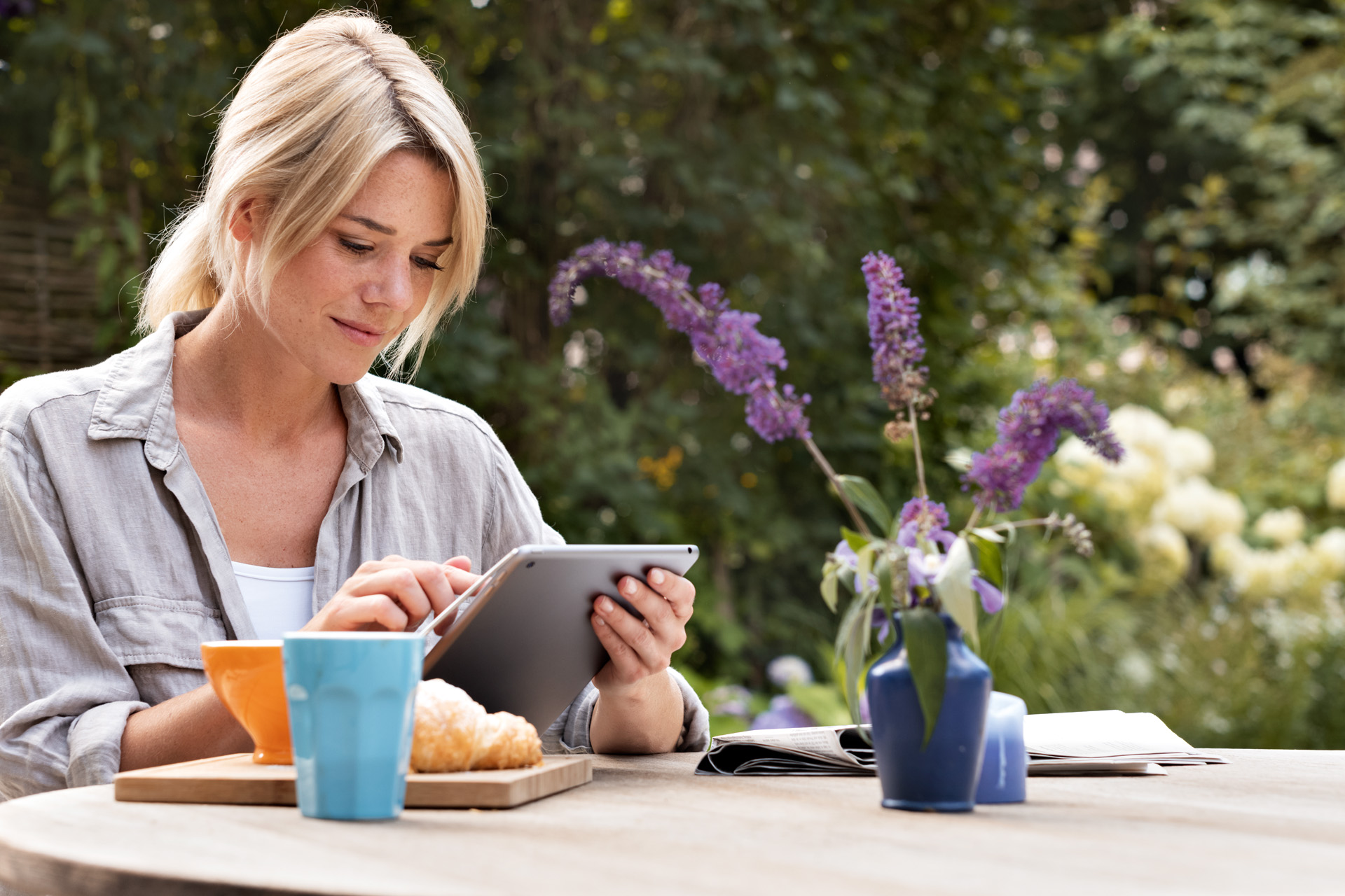 Una mujer utiliza una tableta en la mesa del jardín