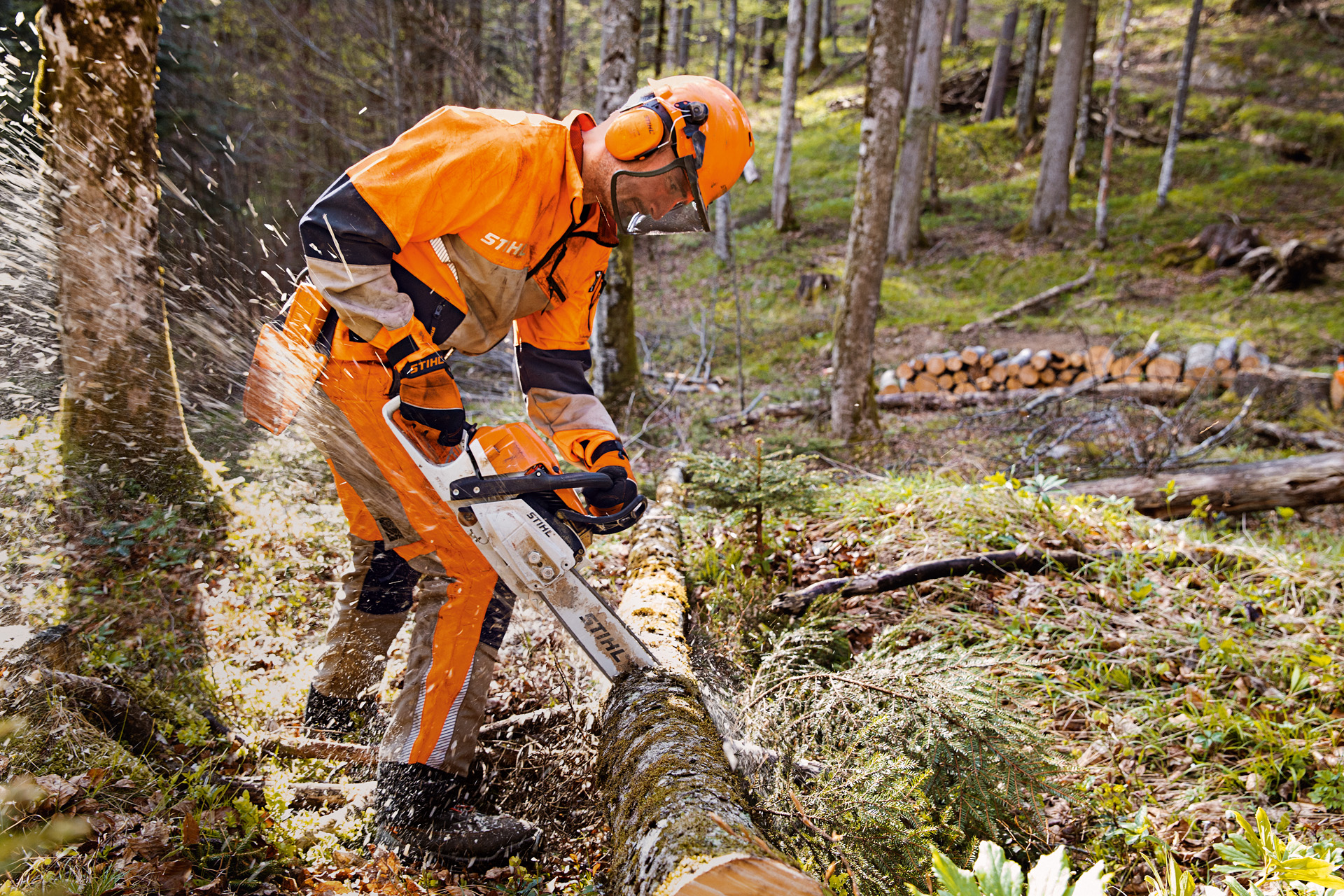 Un hombre con ropa de protección para motosierras con pantalones Dynamic Vent cortando madera con una motosierra STIHL.