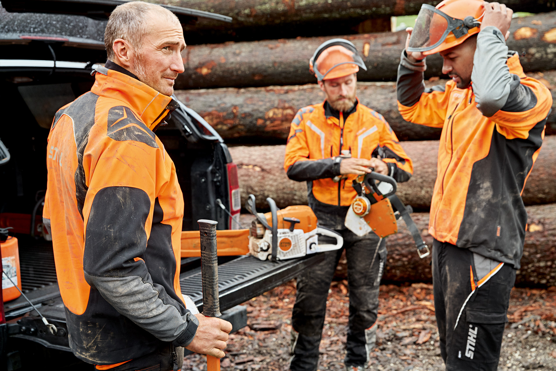 Tres trabajadores forestales con equipo de protección personal frente a un tronco en el bosque.