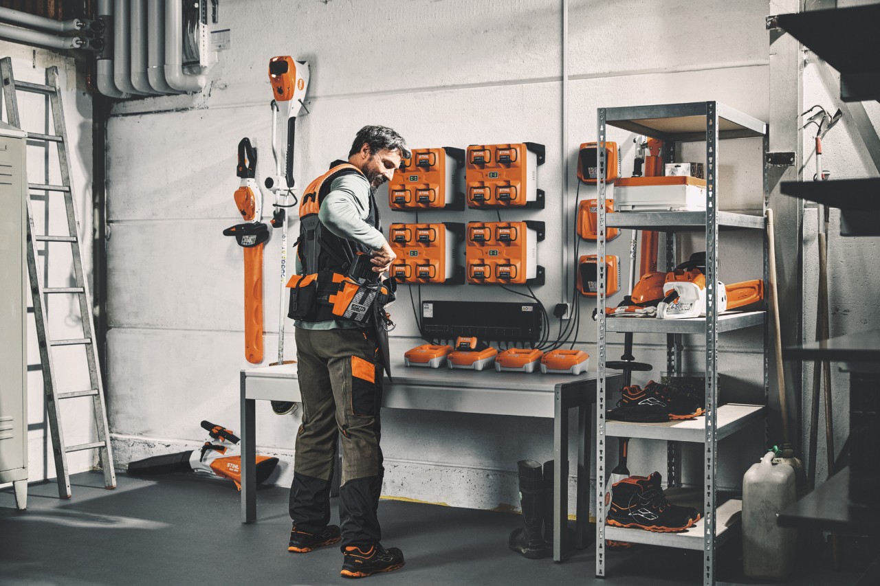 Un hombre en un almacén con máquinas y baterías STIHL llevando el sistema de arnés modular STIHL ADVANCE X-Flex 